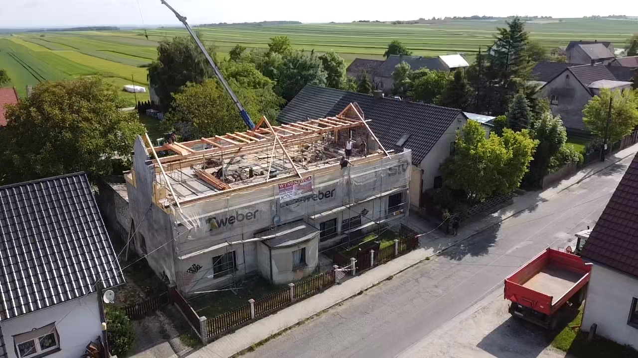 Demontaż starego dachu i przygotowanie konstrukcji pod nowy dach na dwupiętrowym domu z użyciem dźwigu, widoczna reklama Weber na rusztowaniu.