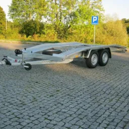 Pusta, srebrna przyczepa samochodowa na parkingu z kostki brukowej, znak parkingu w tle.