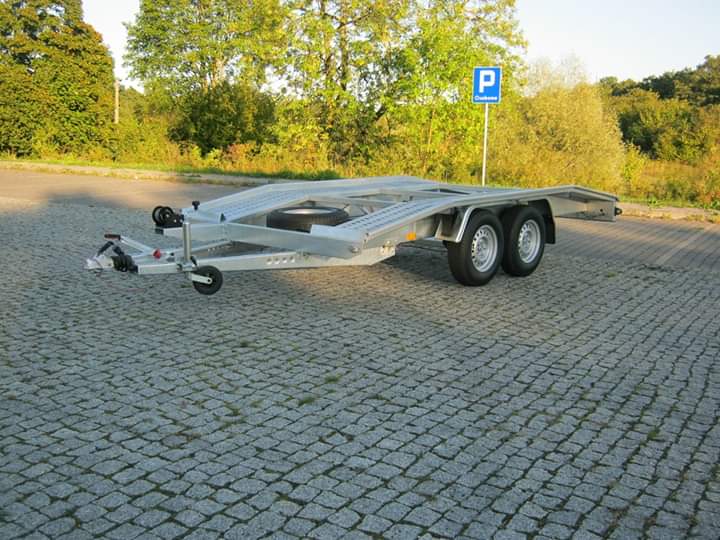 Pusta, srebrna przyczepa samochodowa na parkingu z kostki brukowej, znak parkingu w tle.