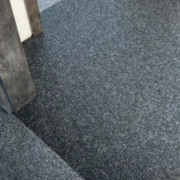 Szara wykładzina dywanowa na podłodze i schodach, widok z góry, fragment betonowej futryny drzwi.