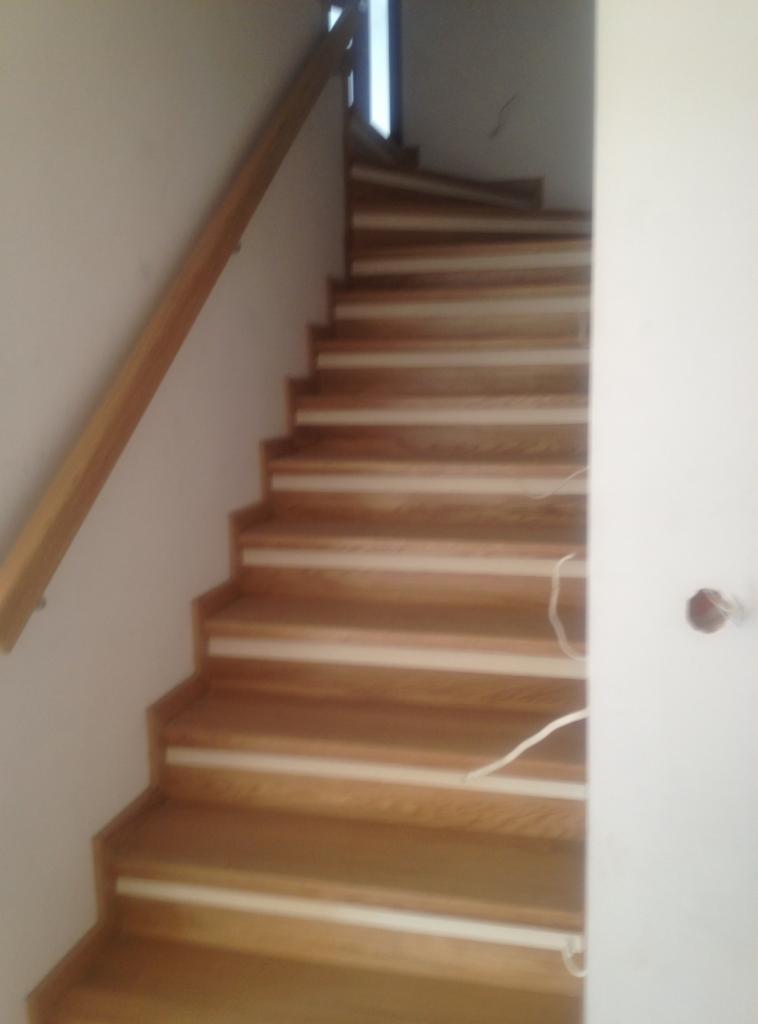 Spiralne schody z jasnego drewna z drewnianą poręczą, widok z dołu, w tle okno.