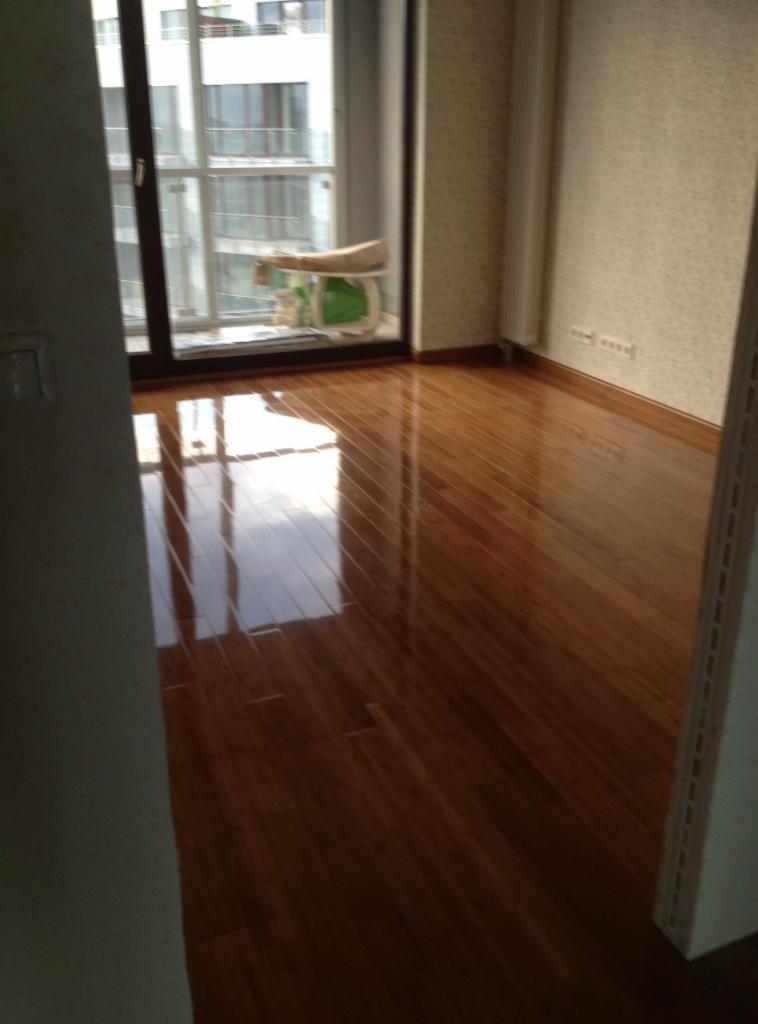 Błyszcząca, nowa drewniana podłoga w pokoju z widocznym oknem i grzejnikiem, odbijająca światło.