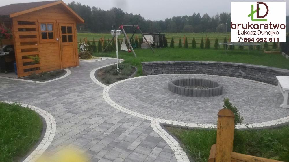 Ułożona kostka brukowa w ogrodzie z paleniskiem, ścieżką do domku narzędziowego i huśtawką w tle, wykonana przez brukarstwo-dunajko.