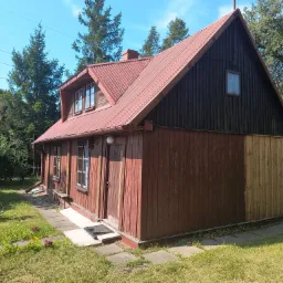 Częściowo odnowiony drewniany dom z czerwoną blachodachówką, gdzie widać różnicę w kolorze desek po piaskowaniu i przed piaskowaniem.