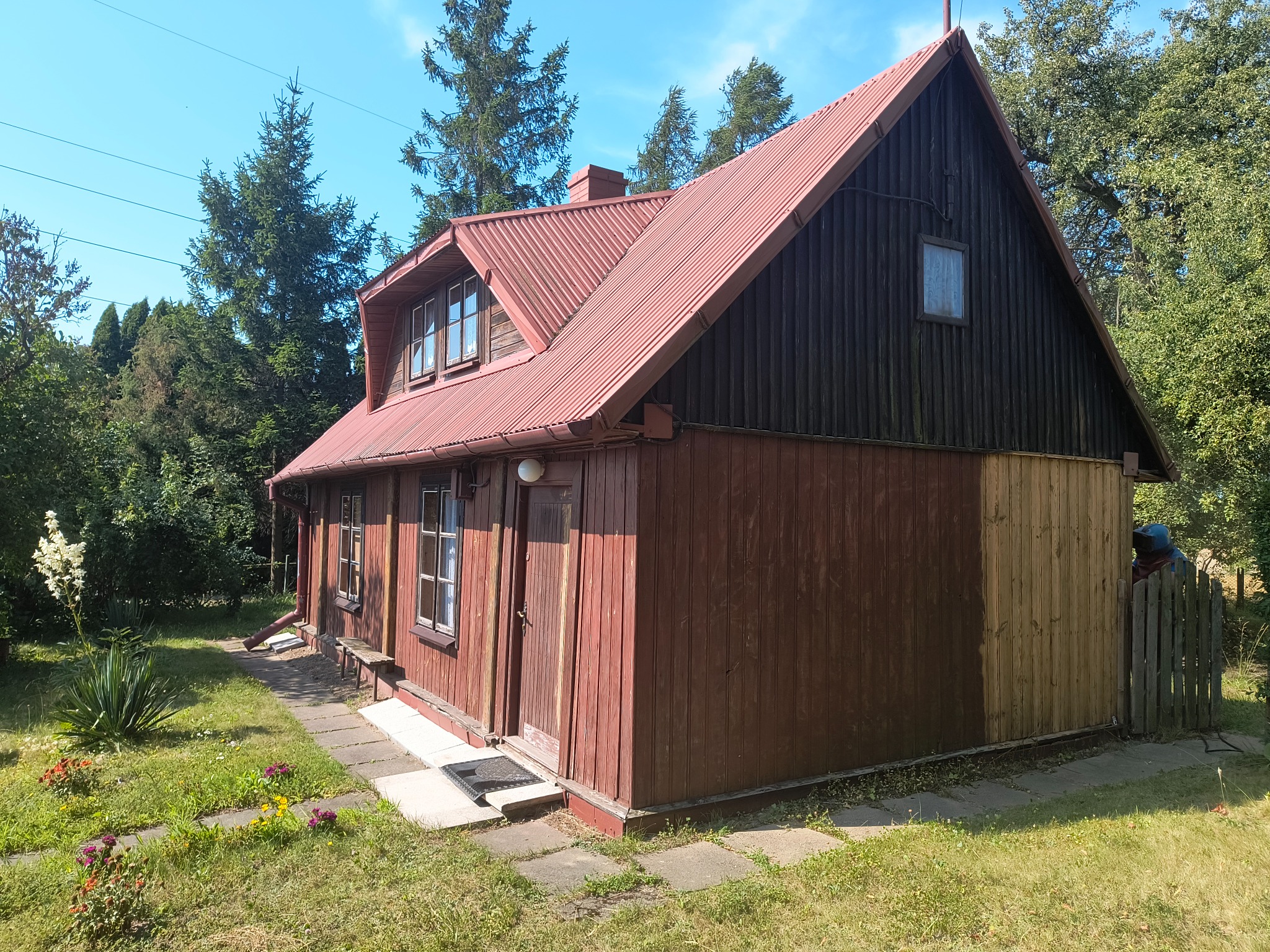 Częściowo odnowiony drewniany dom z czerwoną blachodachówką, gdzie widać różnicę w kolorze desek po piaskowaniu i przed piaskowaniem.