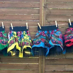 Siedem kolorowych, wzorzystych spódniczek z czarnym tiulem, suszących się na sznurku przypiętych klamerkami na tle drewnianego płotu.