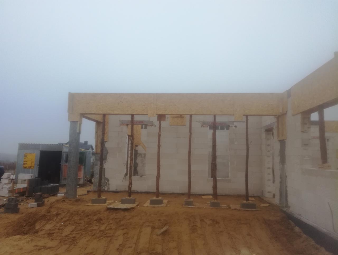 Wznoszenie ścian z betonu komórkowego, podparte drewnianymi stemplami i deskowaniem stropu, widoczne bloczki na zewnątrz budynku.