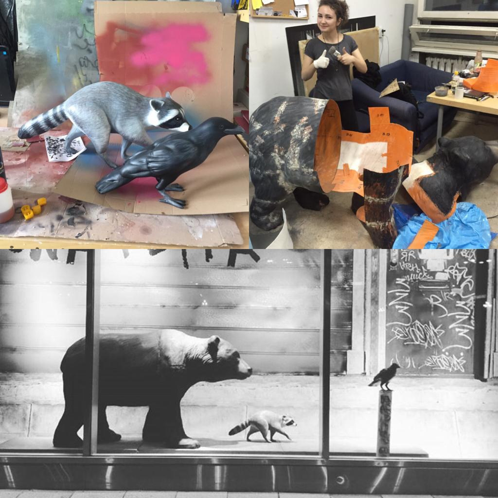 Fotografia przedstawia proces tworzenia dekoracji: malowany szop pracz i kruk na kartonie, częściowo wykończona rzeźba zwierzęcia oraz czarno-biała fotografia niedźwiedzia, szopa i kruka za szybą.