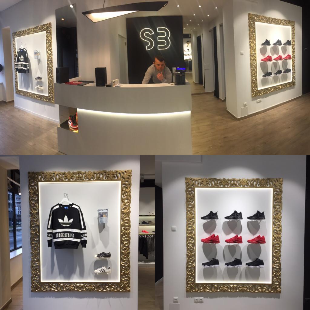 Wnętrze sklepu odzieżowego w Warszawie z elementami dekoracyjnymi w postaci złotych ram, ekspozycja ubrań i obuwia sportowego na ścianach, za ladą sprzedawca.