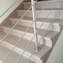 Schody wykończone panelami z metalową balustradą, widok z dołu, z ciemnymi drzwiami w tle.