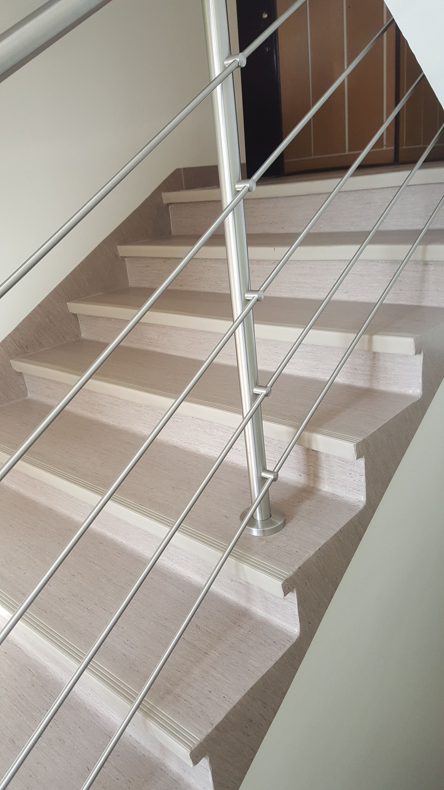 Schody wykończone panelami z metalową balustradą, widok z dołu, z ciemnymi drzwiami w tle.