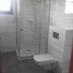 Nowoczesna łazienka z kabiną prysznicową i podwieszaną toaletą, wykończona szarymi płytkami imitującymi marmur, widok z perspektywy podłogi.