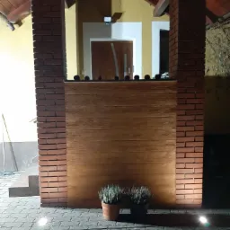 Oświetlony fragment elewacji z ceglanymi filarami i drewnianym panelem, uzupełniony donicami z lawendą, widziany nocą z niskiej perspektywy.