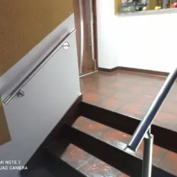 Metalowa poręcz schodowa zamontowana wewnątrz budynku w Jaworach, widoczne brązowe płytki na podłodze i schodach, ściana pomalowana na żółto w górnej części.