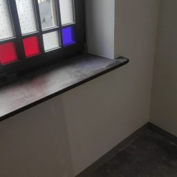 Firma Handlowo-Usługowa Marek Woźniak - Wykończone wnętrze: świeżo pomalowana ściana w jasnym odcieniu, ciemny parapet z kolorowymi szybkami w oknie. Widok na budynek z zewnątrz.
