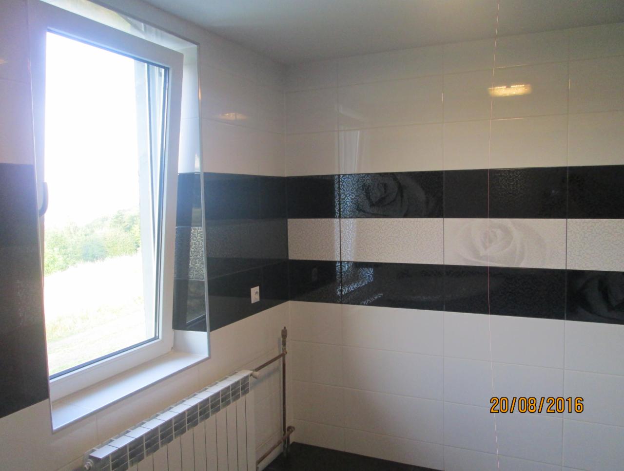 Wykończona łazienka z czarno-białymi płytkami z motywem róży, widok na okno z grzejnikiem pod spodem, data wykonania zdjęcia widoczna w prawym dolnym rogu.