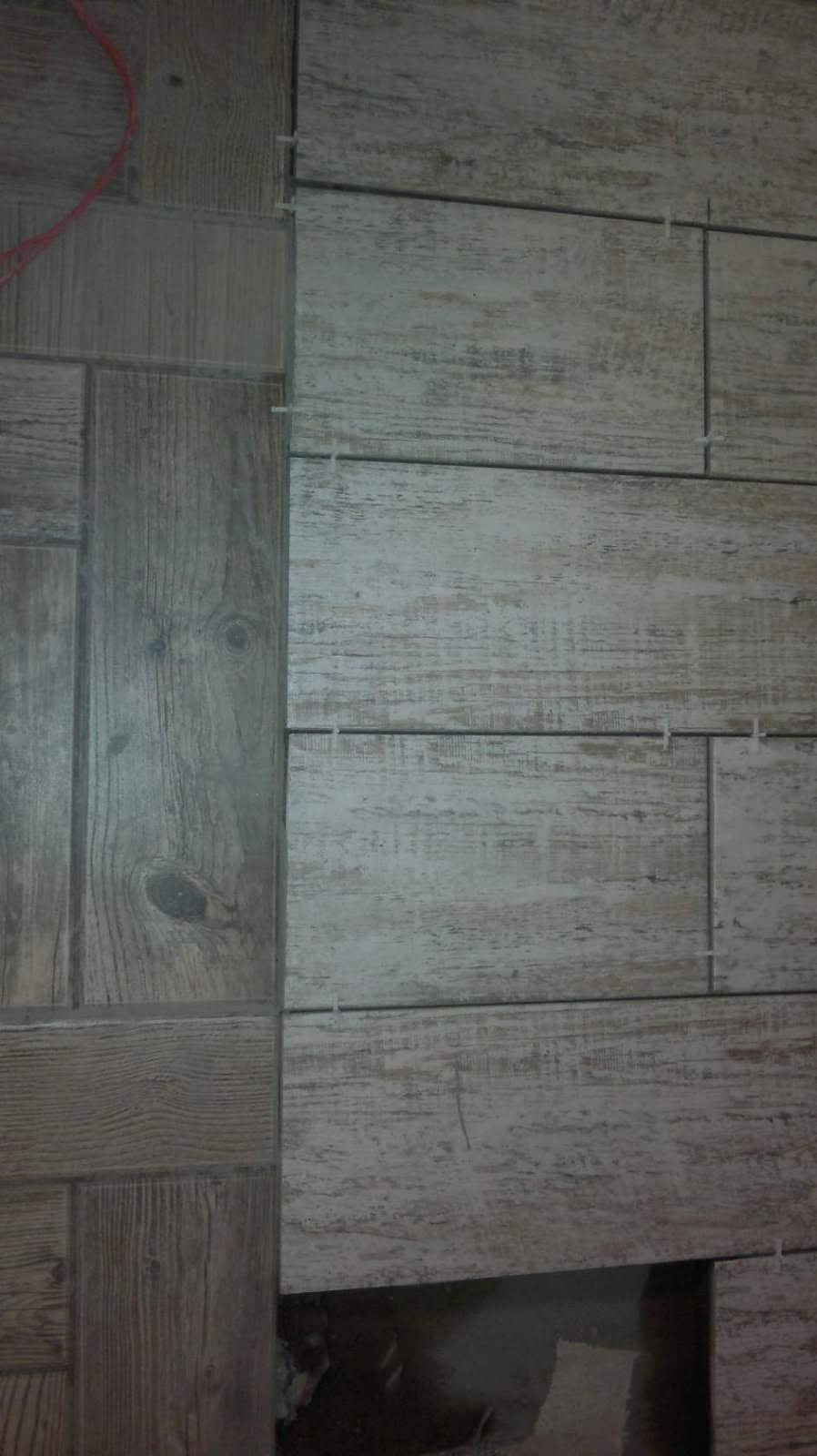 Układanie podłogi z płytek imitujących drewno, widoczne krzyżyki dystansowe i fragment instalacji elektrycznej oraz niedokończony fragment podłogi.