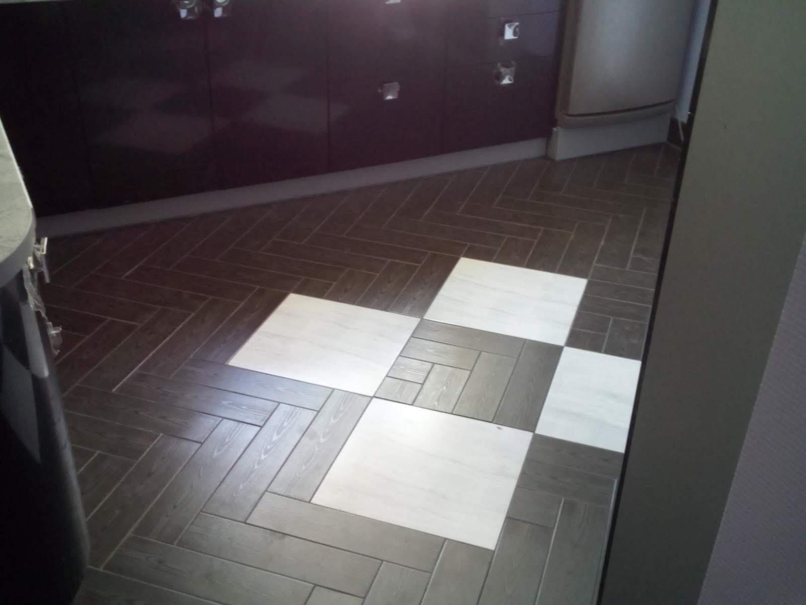 Ułożona podłoga w kuchni z płytek imitujących drewno w ciemnych odcieniach szarości i brązu, przeplatana białymi kwadratowymi płytkami, widoczne dolne szafki kuchenne w kolorze ciemnej śliwki...