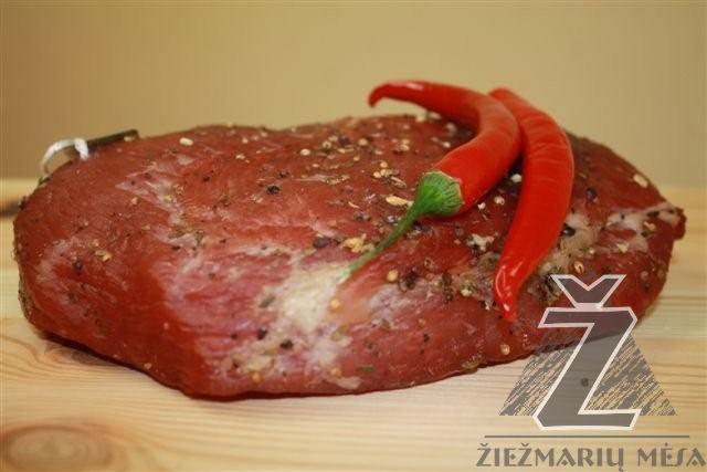 Kawałek peklowanej wołowiny posypany przyprawami, z dwoma czerwonymi papryczkami chili na wierzchu, leżący na drewnianej desce z widocznym logo producenta.