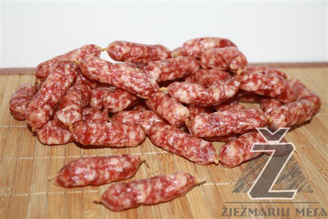 Kiełbaski wieprzowe w naturalnej osłonce ułożone w stos na drewnianej desce z widocznym znakiem wodnym firmy.