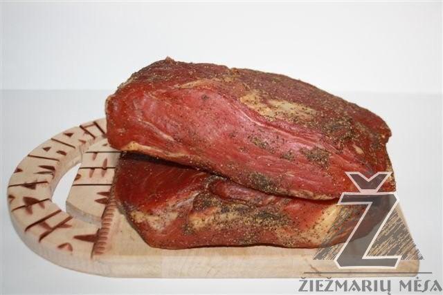 Dwa kawałki wędzonego, przyprawionego mięsa ułożone jeden na drugim na drewnianej desce z uchwytem o zdobieniach w stylu etnicznym, z logotypem producenta w prawym dolnym rogu.