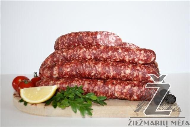 Stos surowych kiełbas na drewnianej desce, udekorowany ćwiartką cytryny, gałązkami zielonej pietruszki i kilkoma pomidorkami koktajlowymi, na białym tle.