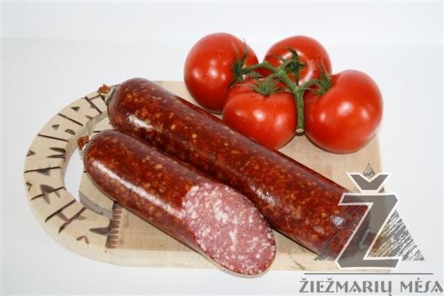 Dwie wędzone kiełbasy na drewnianej desce z dekoracyjnym uchwytem, obok cztery czerwone pomidory na gałązce, w tle białe tło.