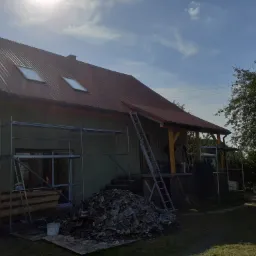 Dom w trakcie renowacji dachu z nowymi oknami dachowymi, rusztowania przy elewacji, sterta starych dachówek na ziemi, drabina oparta o dach.