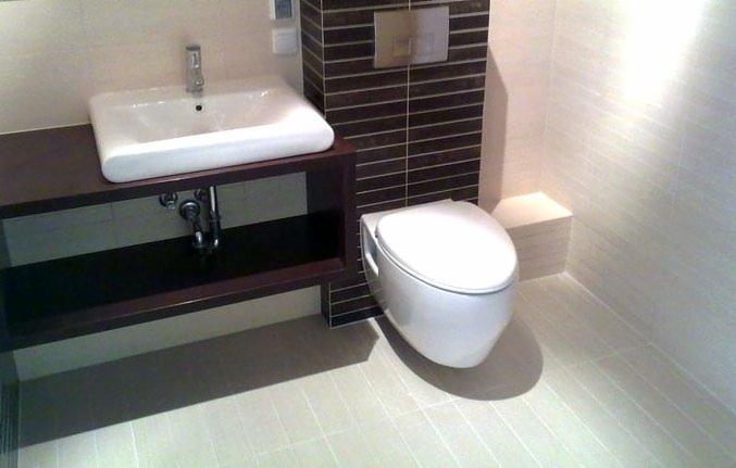 Nowoczesna łazienka z podwieszaną toaletą, umywalką nablatową na ciemnym blacie i płytkami imitującymi drewno na ścianie.