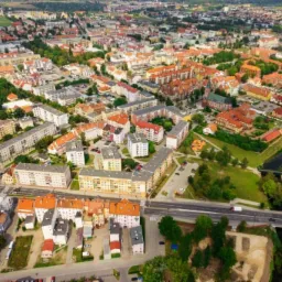 Panoramiczny widok z lotu ptaka na miasto z budynkami mieszkalnymi o zróżnicowanej architekturze, parkiem z rzeką i ruchliwą drogą.