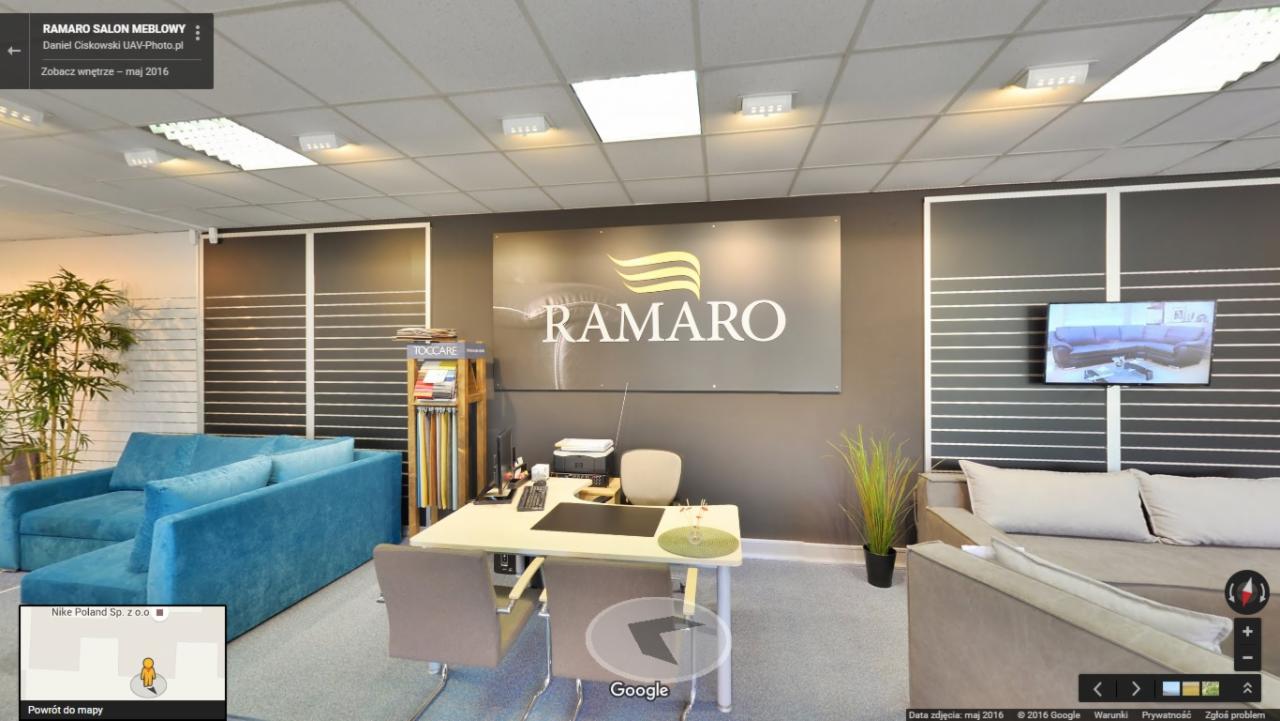 Wnętrze salonu meblowego Ramaro z ekspozycją sofy w odcieniach błękitu, biurkiem z komputerem i telewizorem prezentującym inny model sofy