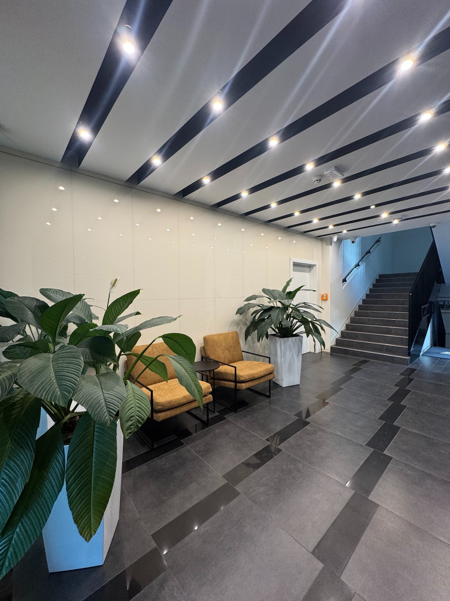 Wnętrze biura po sprzątaniu: lśniąca podłoga z płytek, minimalistyczne meble wypoczynkowe, rośliny doniczkowe i nowoczesne oświetlenie sufitowe.