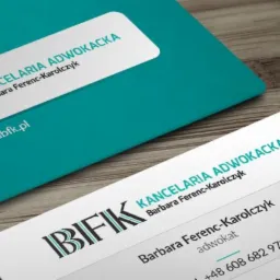 Dwie wizytówki kancelarii adwokackiej na drewnianym tle, jedna w kolorze turkusowym, druga biała z danymi kontaktowymi adwokata.