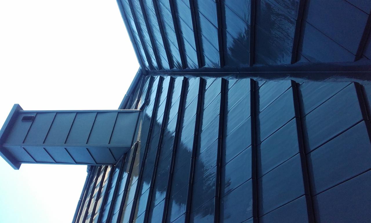 Nowoczesne krycie dachu blachą na rąbek stojący w kolorze grafitowym z widoczną obróbką blacharską komina, ujęcie z dołu.