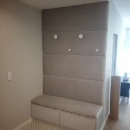 Wnęka z tapicerowanym panelem ściennym, siedziskiem i szafkami w przedpokoju, z trzema okrągłymi wieszakami i wzorzystą podłogą.