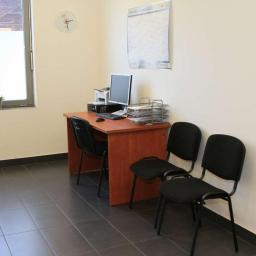 Centrum Zdrowia Psychicznego CZP Tychy - Wnętrze poczekalni: biurko z komputerem, drukarką i organizerem na dokumenty, dwie czarne krzesła dla pacjentów, kalendarz na ścianie, roślina doniczkowa na parapecie.