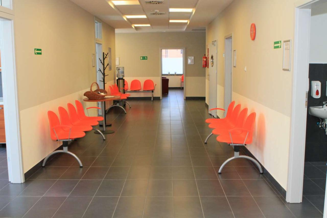 Korytarz w prywatnej klinice z pomarańczowymi krzesłami, dystrybutorem wody i koszem na stoliku.