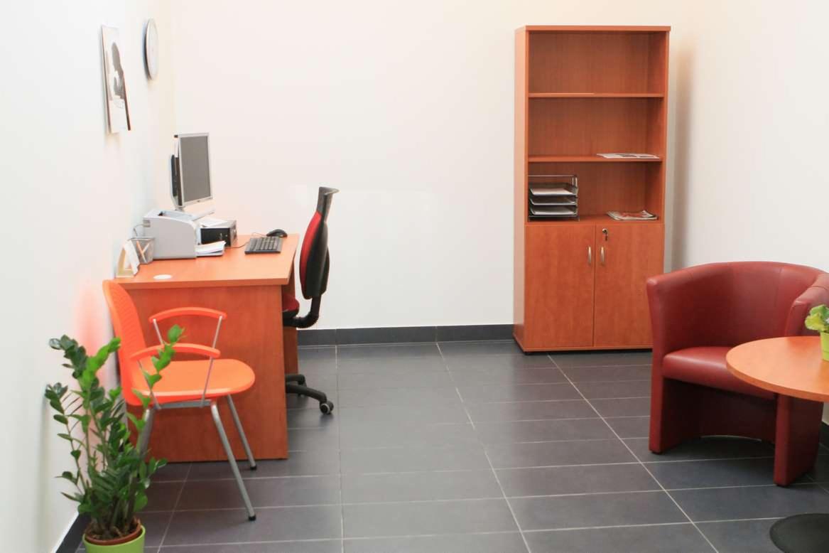 Wnętrze gabinetu lekarskiego w Tychach: biurko z komputerem, krzesło biurowe, pomarańczowe krzesło dla pacjenta, regał na dokumenty i czerwony fotel dla pacjentów.