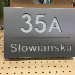 Metalowa tabliczka adresowa z numerem 35A i nazwą ulicy Słowiańska, wycięta laserowo, na drewnianym blacie.