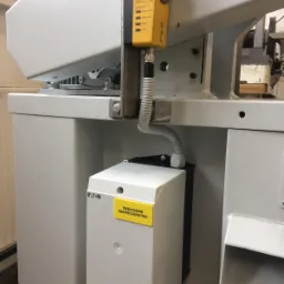 Żółty czujnik bezpieczeństwa Pilz zamontowany na szarej maszynie przemysłowej, z białym przekaźnikiem bezpieczeństwa Eaton pod spodem, połączone kablem w peszlu.