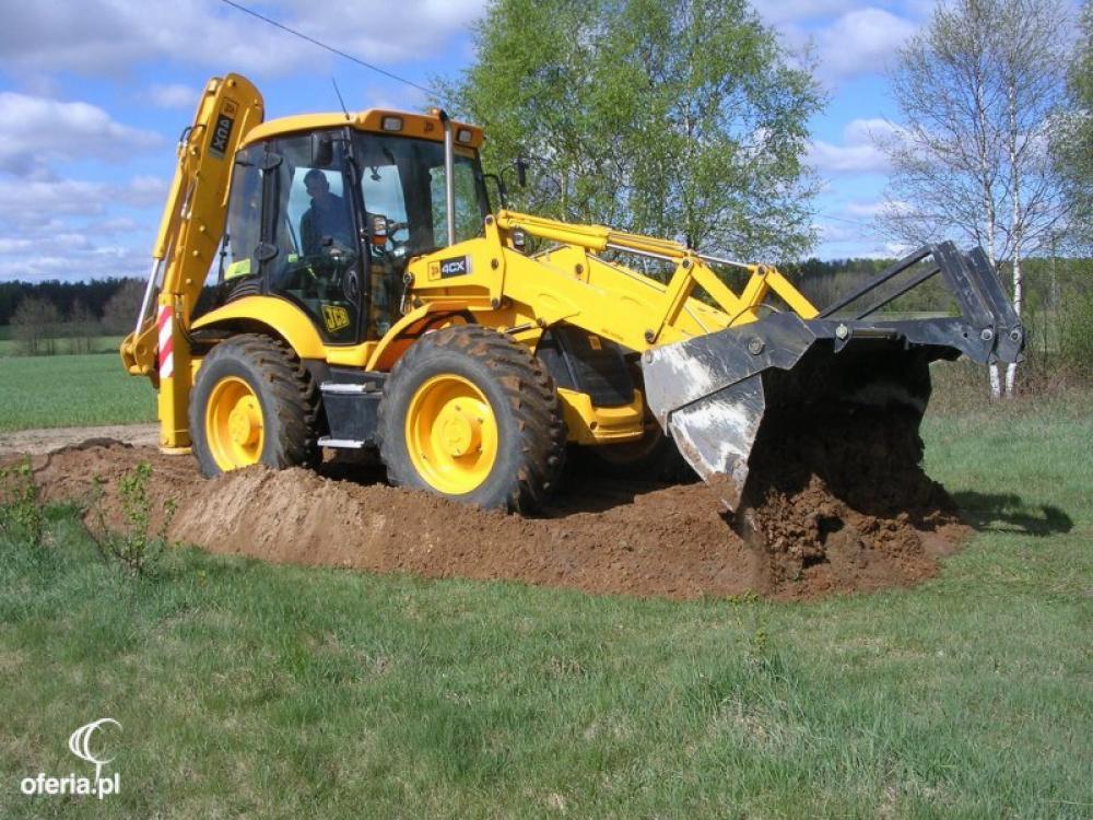 Żółta koparko-ładowarka JCB 4CX w trakcie prac ziemnych na trawiastym terenie, widoczna świeżo usypana pryzma ziemi.