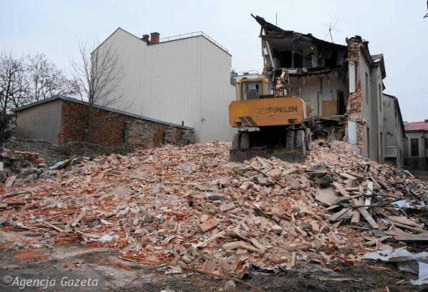 Żółta spycharka Zeppelin na tle częściowo zburzonego budynku, gruzowisko cegieł i elementów konstrukcyjnych.