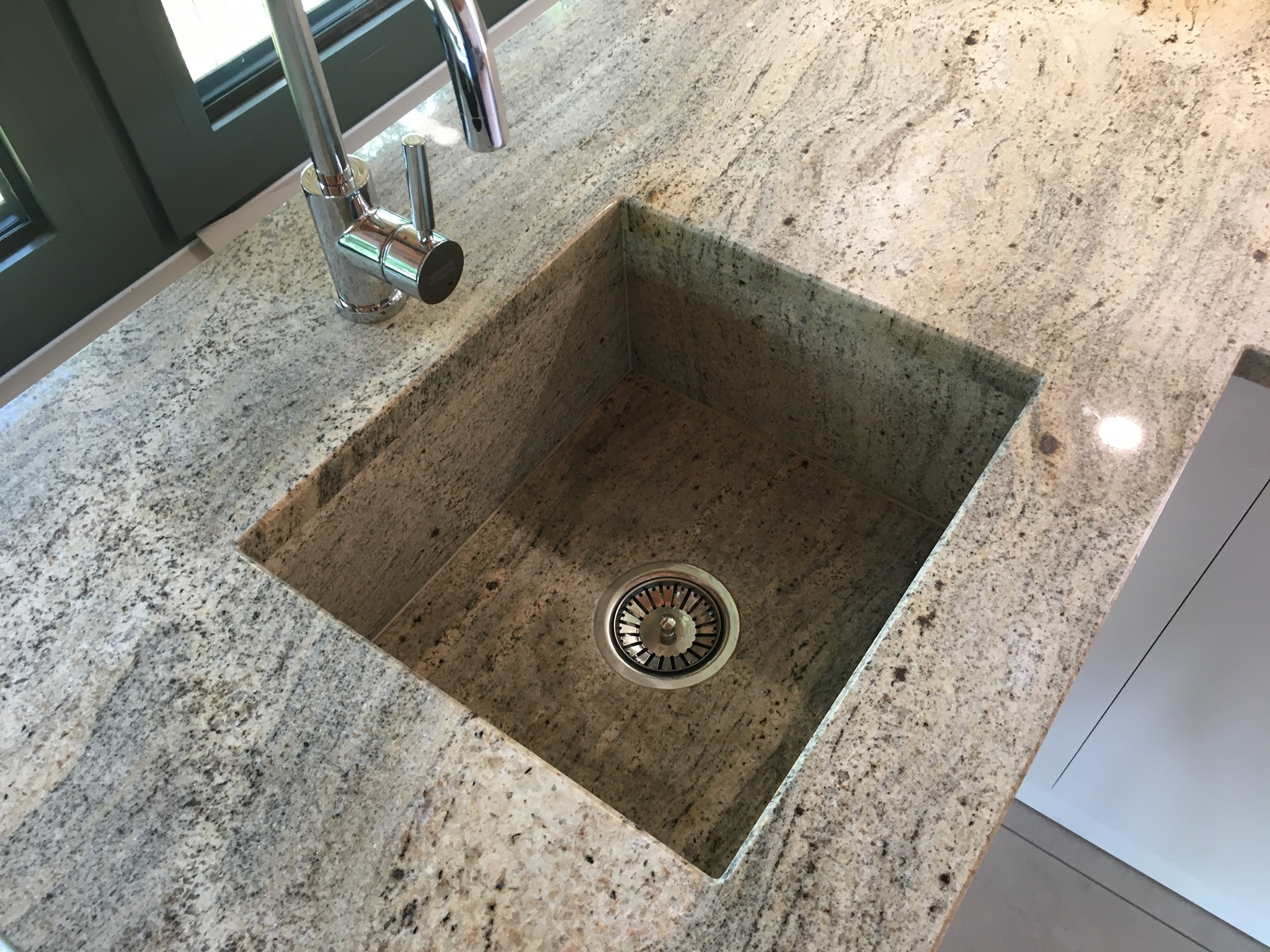 Jasny, nakrapiany blat kuchenny z zamontowanym zlewem i chromowaną baterią, widok z góry.