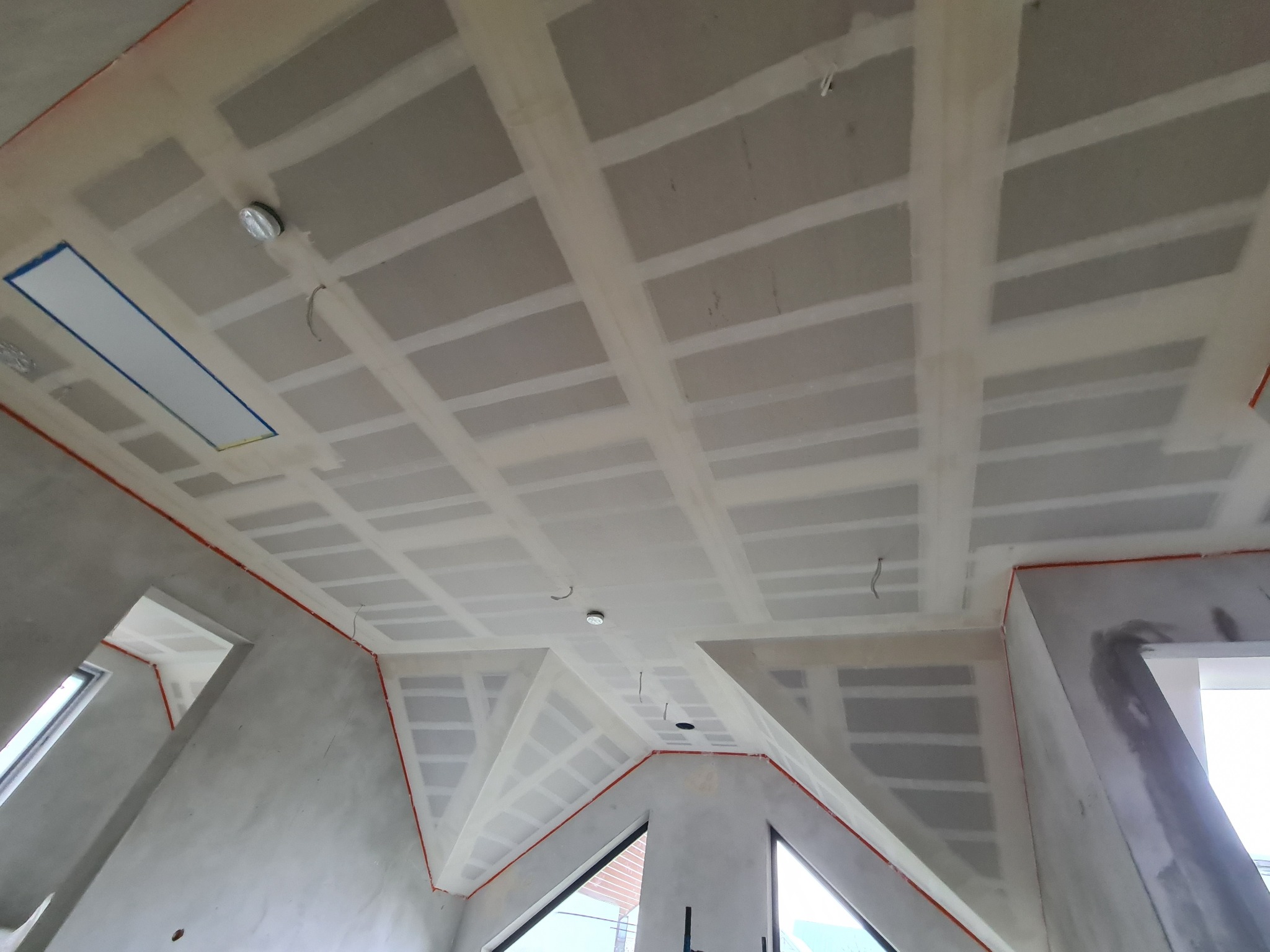 Sufit z płyt kartonowo-gipsowych na metalowej konstrukcji, widoczne łączenia płyt zaszpachlowane i przygotowane do malowania, instalacja elektryczna w suficie podwieszanym, ściany surowe.