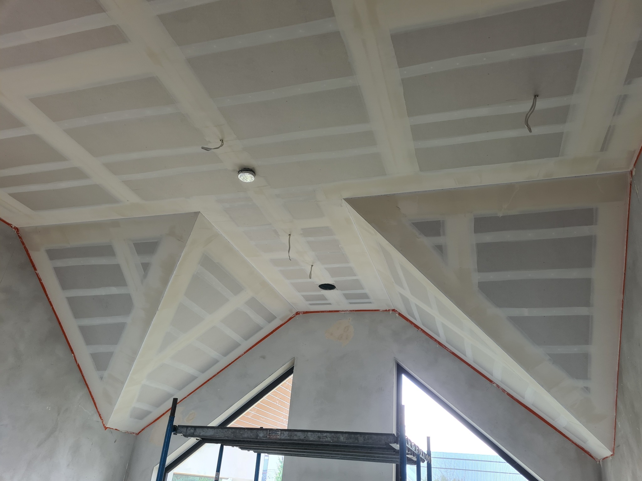 Skośny sufit poddasza w trakcie montażu płyt, widoczne łączenia wzmocnione taśmą, przygotowany otwór na oświetlenie, fragment rusztowania w dolnej części kadru.