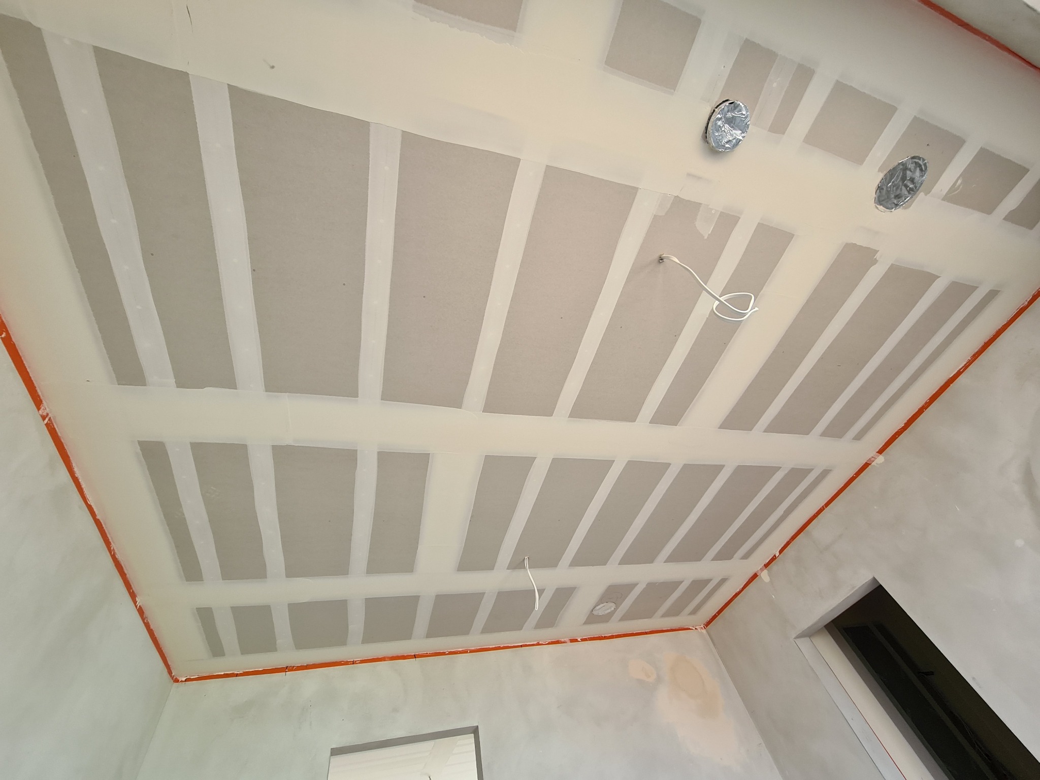 Sufit w trakcie montażu z widocznymi płytami, maskowaniem łączeń taśmą i przygotowaniem do instalacji oświetlenia, obrysowany pomarańczową taśmą malarską.