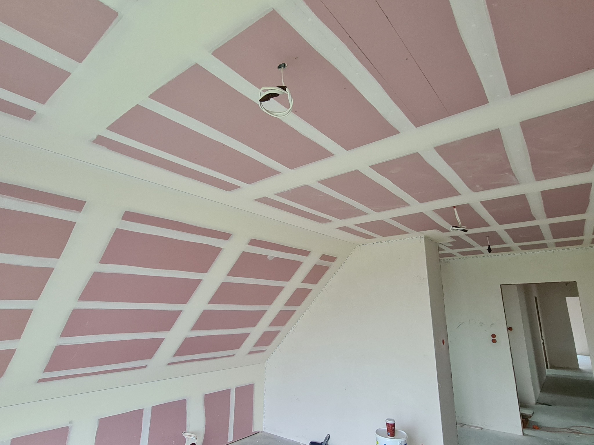 Montaż płyt gipsowo-kartonowych na poddaszu, widoczne profile i płyty w kolorze różowym, przygotowane do dalszych prac wykończeniowych, z widocznymi przewodami elektrycznymi.