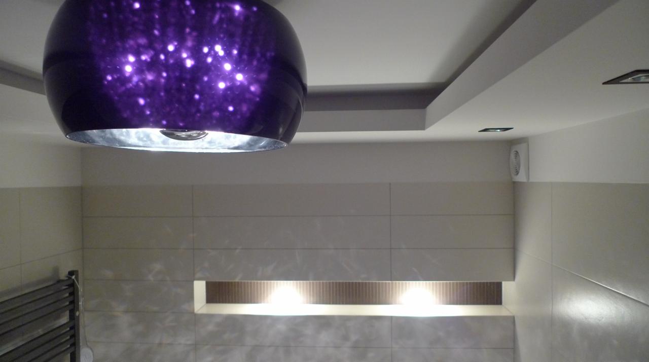 Lampa sufitowa w odcieniach fioletu z efektem gwiazd, oświetlająca wykończoną łazienkę z podświetlaną wnęką i grzejnikiem drabinkowym