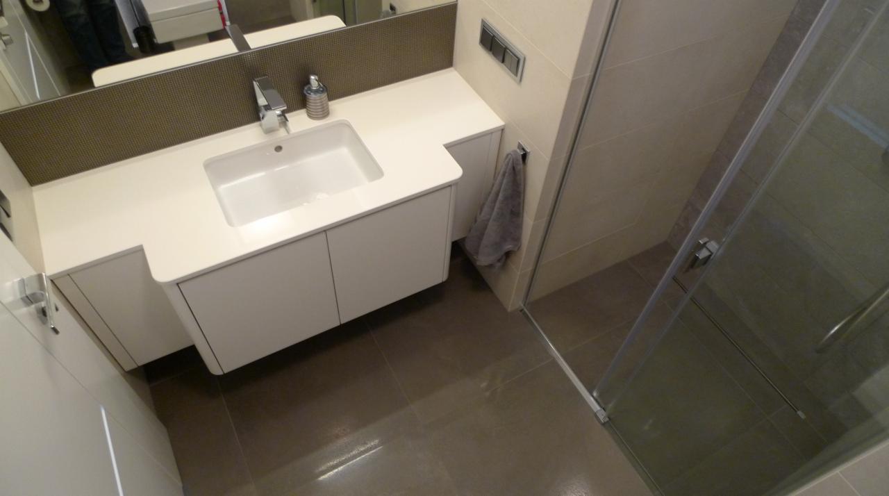 Nowoczesna łazienka z białą szafką pod umywalką, szarą podłogą z płytek i kabiną prysznicową ze szklanymi drzwiami, widok z góry.