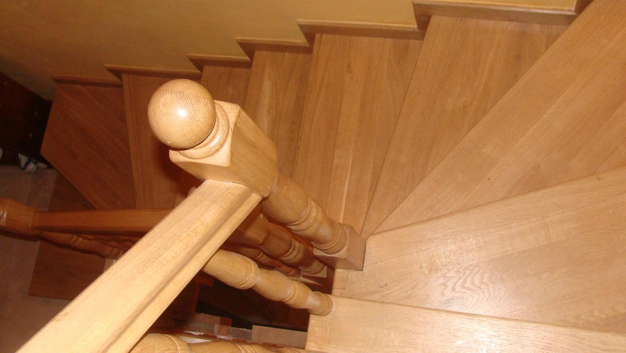 Drewniane schody spiralne z jasnego drewna, widok z góry na poręcz z okrągłym zakończeniem.